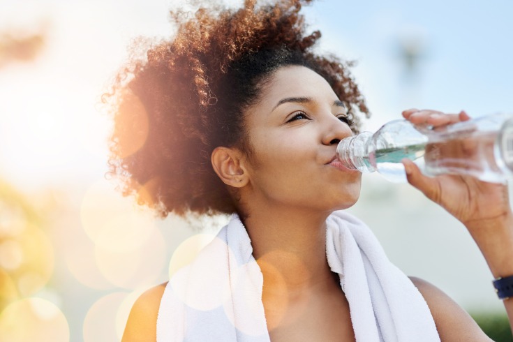  Young woman drinking from a bottle of water to stay hydrated after exercising outside.