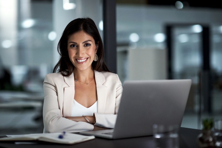 Female executive sitting confidently on her desk with her laptop in front.