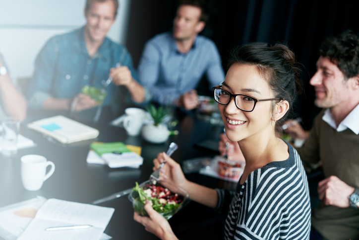 Happy employees eating lunch together as part of a health and wellbeing exercise