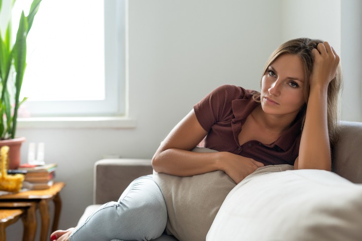 Young women sitting on her couch struggling with mental health due to her ongoing injury rehabilitation