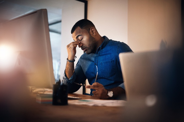 Man showing symptoms of burnout while working late to finish his tasks.