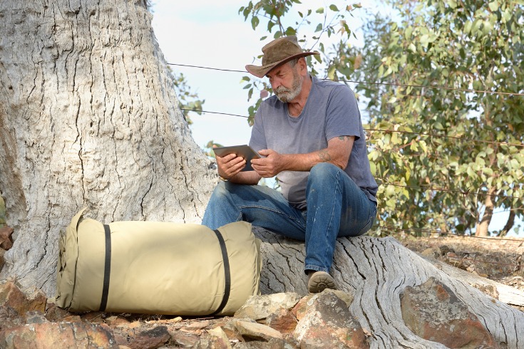 Man using a tablet to research mental health services available to him in rural Australia while sitting on a tree trunk.