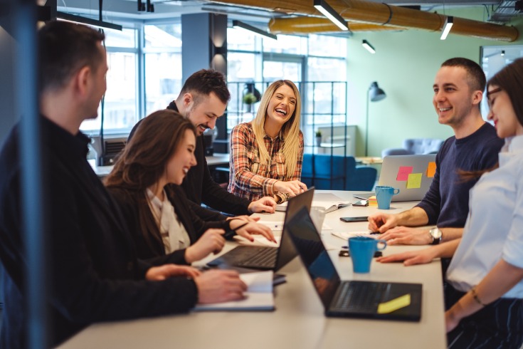 Employees laughing and interacting during a meeting at their mentally healthy workplace.