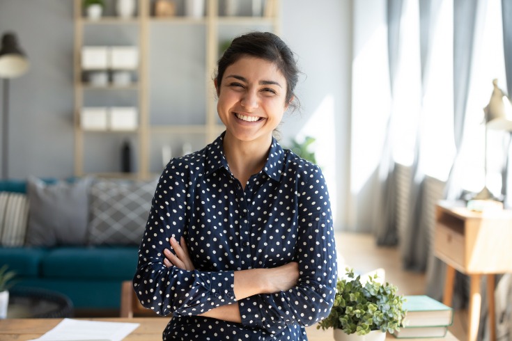 A woman standing with her arms crossed and smiling at the camera in a living room.