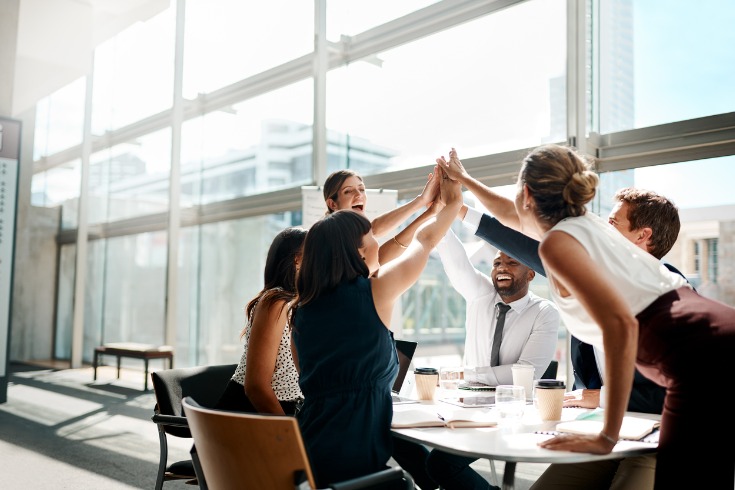 Workers sitting at a table during a meeting and celebrating their success as a team.