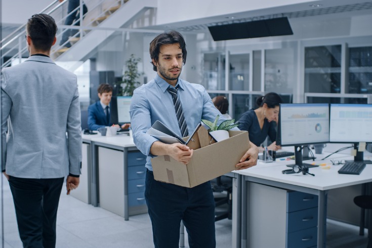 Businessman walking out of the office with a box of belongings after losing his job.